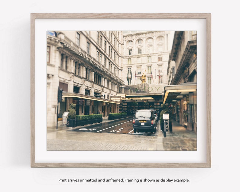 May include: A black taxi cab is parked in front of a grand building with the word "SAVOY" above the entrance. The building has a classic architecture with tall windows and ornate details. The scene is captured in a vintage style with a soft, faded color palette.