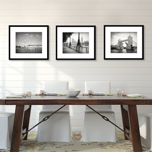 Op de afbeelding: Drie zwart-wit geframed foto's van Londense bezienswaardigheden. De foto's hangen aan een witte muur boven een houten eettafel met vier witte stoelen.