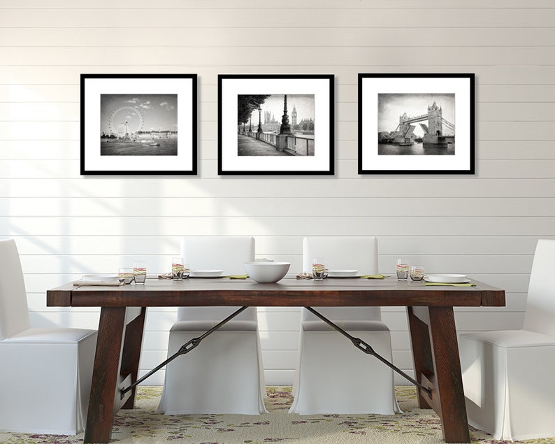 Op de afbeelding: Drie zwart-wit geframed foto's van Londense bezienswaardigheden. De foto's hangen aan een witte muur boven een houten eettafel met vier witte stoelen.