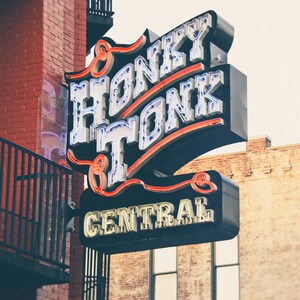 May include: A neon sign with the words "Honky Tonk Central" in white letters with red outlines. The sign is mounted on a brick building.