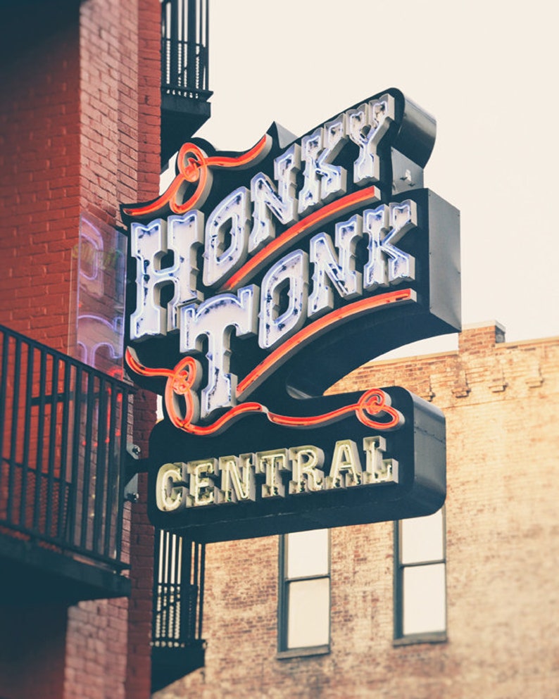 May include: A neon sign with the words "Honky Tonk Central" in white letters with red outlines. The sign is mounted on a brick building.