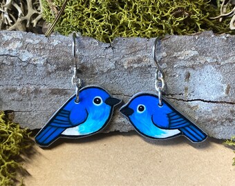 May include: A pair of bluebird earrings with silver hooks. The bluebirds are painted with white accents and black details.