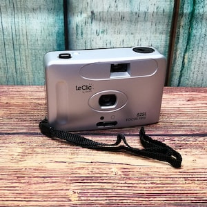 May include: A silver Le Clic by Contax 82SL Focus Free film camera with a black strap.