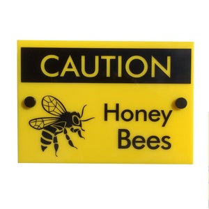 May include: Yellow sign with black text and a black silhouette of a bee. The sign reads "CAUTION Honey Bees".