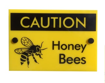 May include: Yellow sign with black text and a black silhouette of a bee. The sign reads "CAUTION Honey Bees".