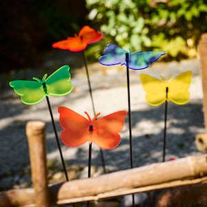 Peut inclure: Plusieurs piquets de jardin en forme de papillon aux couleurs vives. Les papillons sont dans des tons d'orange, de rouge, de vert, de bleu et de jaune. Chaque papillon est monté sur une fine tige noire, créant une décoration extérieure fantaisiste.