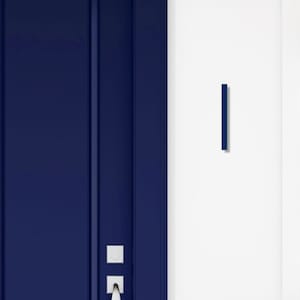 May include: A section of a navy blue door with vertical paneling and a silver handle. A matching navy blue, rectangular door pull is mounted on the adjacent white wall. The door and pull create a modern, minimalist aesthetic.