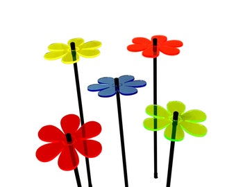 Könnte beinhalten: Fünf bunte Plastikblumen mit schwarzen Stielen. Die Blumen sind gelb, rot, blau und grün.
