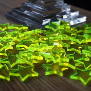 Peut inclure: Des étoiles en acrylique translucide vert néon sont dispersées sur une surface en bois. En arrière-plan, une structure en verre claire à plusieurs niveaux est visible. Les étoiles sont le point central, créant un contraste vif.