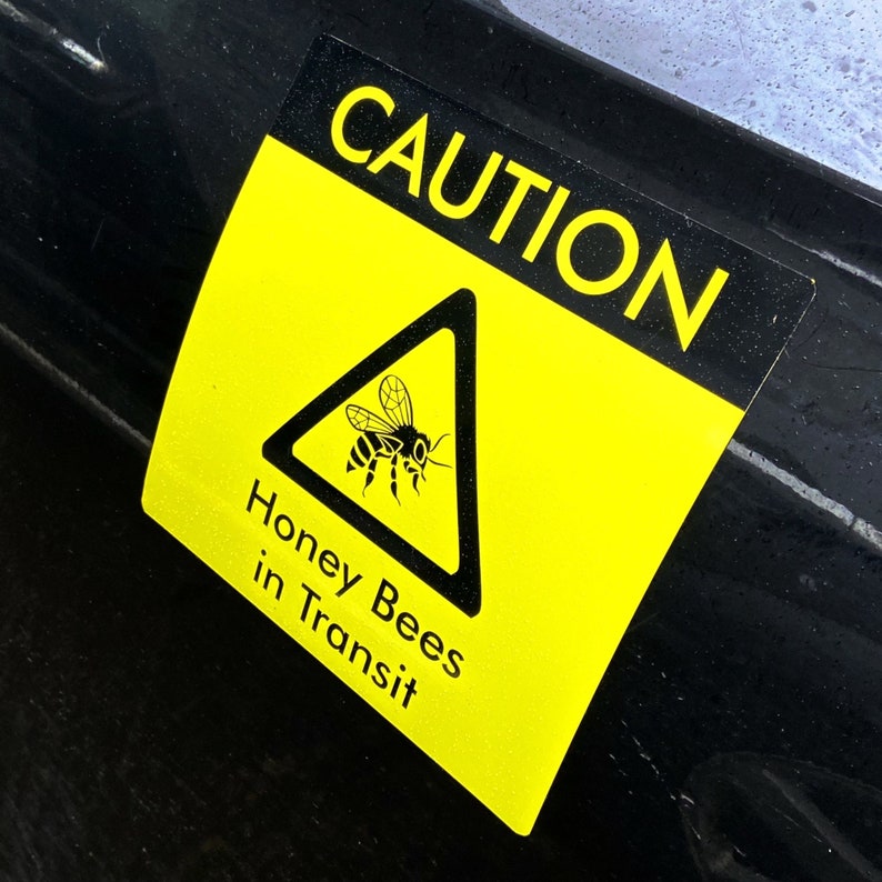 Square Bees in Transit Sign, made of magnetic material with outdoor use vinyl finish, this long lasting sign is ideal for repeated use on vans, cars and other forms of transport to warn of your precious cargo. Image shows sign clipped onto the side of a car. This can be used in the same way as an L Plate and can be clipped onto any magnetic surface and also safely removed and used repeatedly.
