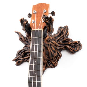 May include: A wooden ukulele wall mount shaped like a tree trunk with a ukulele hanging from it.