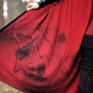 May include: A red cloak with a black border and a dark illustration of a bat and a raven. The cloak is held up, revealing the detailed artwork on the inside. The cloak is part of a gothic or fantasy-themed outfit.