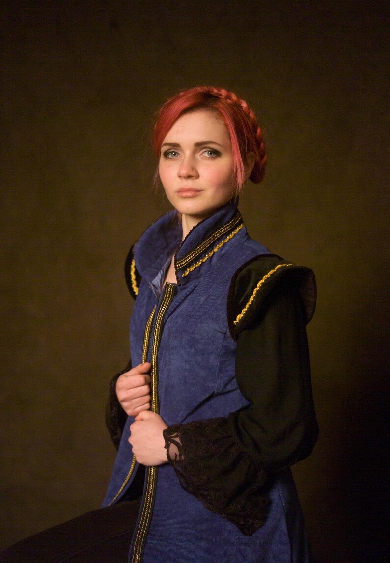 May include: A blue vest with gold trim and black sleeves. The vest has a high collar and a zipper down the front. The sleeves are long and black with lace cuffs. The person in the image has red hair.
