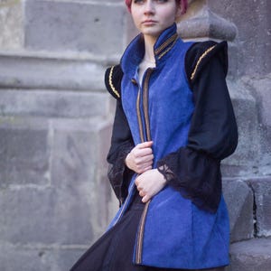 May include: A blue velvet vest with gold trim and black sleeves. The vest has a high collar and a zipper down the front. The sleeves are long and black with lace cuffs. The outfit is paired with a long black skirt.