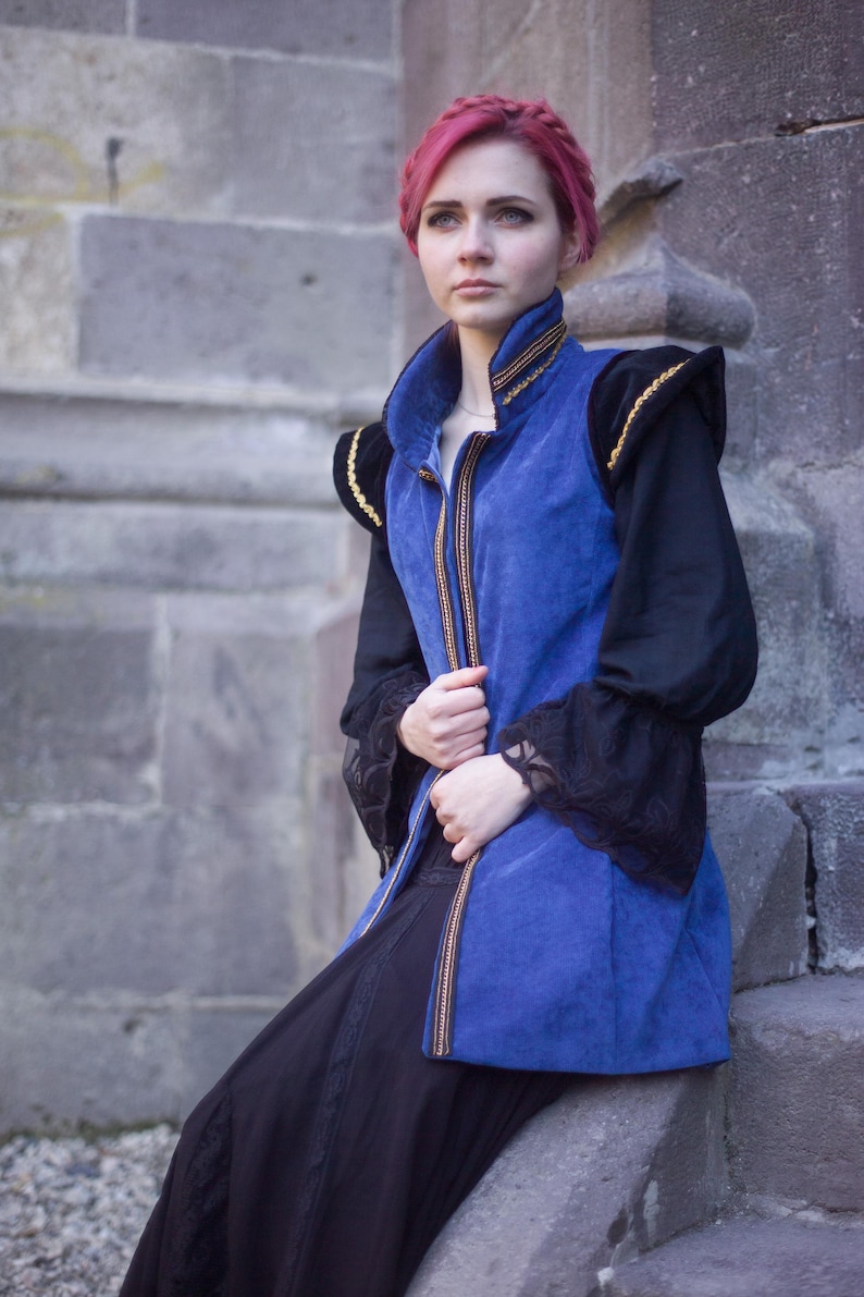 May include: A blue velvet vest with gold trim and black sleeves. The vest has a high collar and a zipper down the front. The sleeves are long and black with lace cuffs. The outfit is paired with a long black skirt.