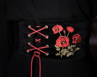May include: A black velvet corset with red poppy embroidery and red laces. The corset has a lace-up front and a decorative design.