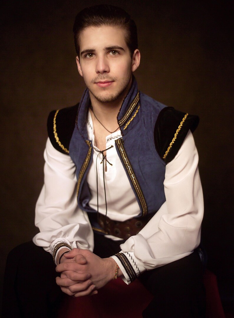 May include: A person wearing a white shirt with a lace-up neckline, a blue vest with gold trim, and black accents. The vest has black shoulder pads with gold trim. The person is wearing a brown belt and black pants.
