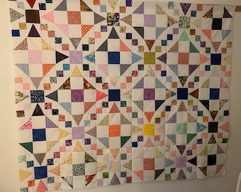 May include: A colorful quilt with a geometric pattern of squares and triangles. The quilt is made up of various fabrics with different patterns and colors, including pink, purple, blue, green, yellow, and orange.