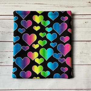 May include: A black fabric item with a repeating pattern of colorful, rainbow-gradient hearts. The hearts vary in size and are outlined in white. The background is black. The item is rectangular and appears to be a sleeve or cover.