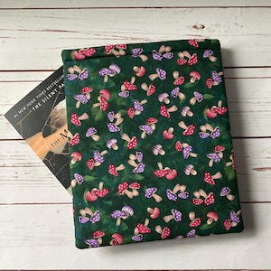 May include: A green fabric book sleeve featuring a pattern of red and purple mushrooms with white polka dots. The book sleeve is partially open, revealing a book with the title "The Silent Patient".