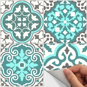 Op de afbeelding: Vier vierkante decoratieve tegels met een zelfklevend ontwerp. Elke tegel heeft een ander sierlijk patroon in teal, wit, grijs en blauwgroen. De tegels zijn gerangschikt in een raster, met een hoek van een tegel die wordt afgepeld.