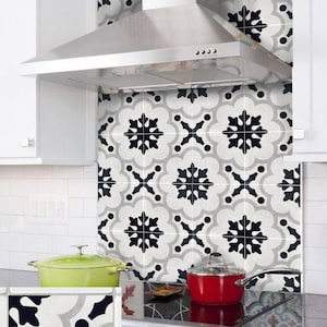 May include: Kitchen backsplash tiles featuring a black and white floral design. The tiles are installed behind a stainless steel extractor hood. A hand is peeling off a tile in the corner, showing the adhesive backing.