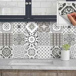 Puede incluir: Azulejos decorativos autoadhesivos con diversos patrones geométricos en tonos grises, blancos y negros. Los azulejos están dispuestos en una cuadrícula, creando un diseño de salpicadero atractivo. Una mano despega un azulejo.