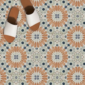 May include: Overhead shot of two white leather slide sandals with brown soles, placed on a patterned tile floor. The floor features a repeating geometric design in shades of orange, blue, and gray.