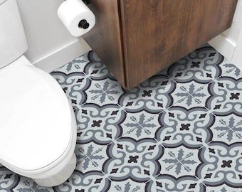 May include: Bathroom floor tiles featuring a repeating pattern in shades of grey and black. The tiles are arranged in a geometric design, with a toilet and a dark wood cabinet visible in the background. The tiles add a decorative element to the bathroom.