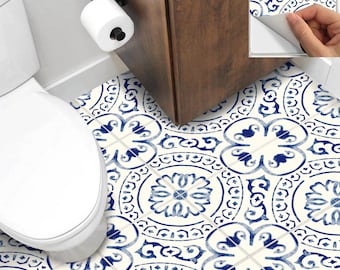 May include: Blue and white patterned peel and stick floor tiles in a bathroom. The tiles feature a floral design. A roll of toilet paper is mounted on the wall. The text "Peel & Stick" is visible.