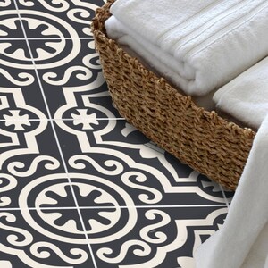 Puede incluir: Una cesta de mimbre tejida llena de toallas blancas dobladas. La cesta est&aacute; sobre un suelo de baldosas estampadas con un dise&ntilde;o geom&eacute;trico negro y crema. Una toalla blanca cuelga del borde de la cesta.