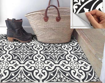May include: Black and white patterned tile flooring with a decorative design. A pair of dark brown ankle boots and a woven basket bag with leather handles are placed on the tiles. A hand peels a tile sticker with a similar pattern.
