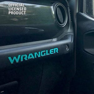 Pode incluir: Detalhe interior de um painel de porta de veículo preto. A palavra "WRANGLER" é exibida em letras turquesas. O canto superior esquerdo apresenta o logotipo MOPAR e o texto "OFFICIAL LICENSED PRODUCT".