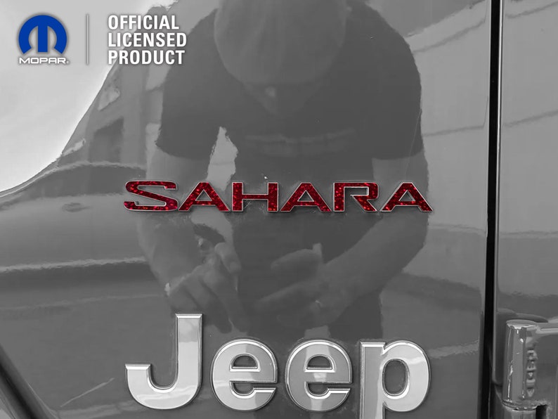 Pu&ograve; includere: Un emblema "SAHARA" rosso glitterato su una Jeep grigia con un emblema "Jeep" argentato sotto. L'immagine &egrave; un primo piano della parte posteriore del veicolo.