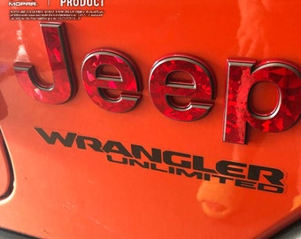 May include: A red Jeep Wrangler Unlimited emblem with a diamond-like pattern. The emblem is attached to a bright orange vehicle. The text "OFFICIAL LICENSED PRODUCT" is visible above the emblem.