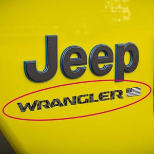 May include: Yellow Jeep Wrangler emblem with black and blue lettering. The word "Jeep" is above "Wrangler", which includes an American flag graphic. The emblem is on a yellow vehicle panel.