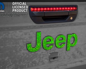 May include: Green glitter Jeep lettering on a gray car tailgate. The tailgate has a black handle and a red brake light. The text "MOPAR. OFFICIAL LICENSED PRODUCT" is visible above the Jeep lettering.