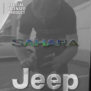 Pu&ograve; includere: Un'immagine in bianco e nero di una Jeep Sahara con un logo Jeep argentato e un logo Sahara iridescente nero e verde. L'immagine &egrave; scattata dal lato del veicolo.