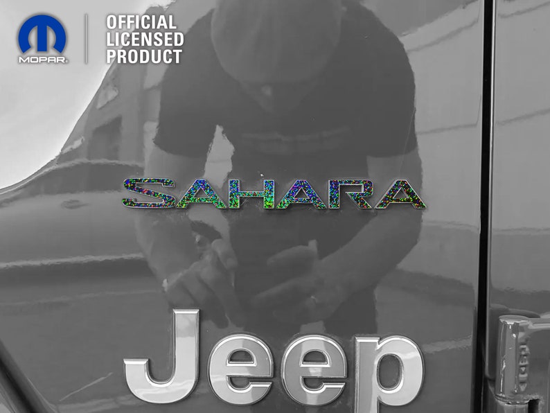 Pu&ograve; includere: Un'immagine in bianco e nero di una Jeep Sahara con un logo Jeep argentato e un logo Sahara iridescente nero e verde. L'immagine &egrave; scattata dal lato del veicolo.