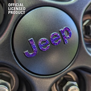 May include: A close-up of a black Jeep wheel cover with a purple and blue glitter Jeep logo. The cover is an official licensed product.
