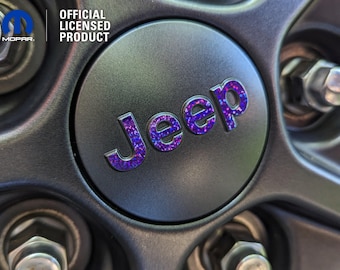 May include: A close-up of a black Jeep wheel cover with a purple and blue glitter Jeep logo. The cover is an official licensed product.