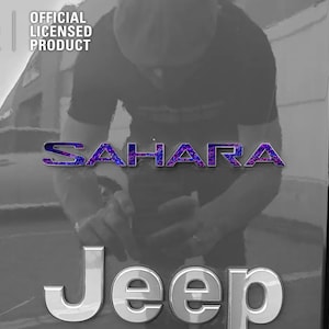 Pu&ograve; includere: Un'immagine in bianco e nero di una Jeep Sahara con un emblema "Sahara" viola e nero sul retro. La Jeep &egrave; un prodotto ufficiale con licenza.
