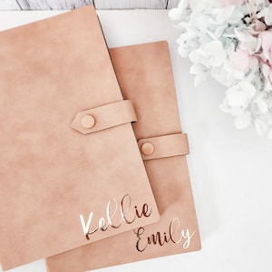 May include: Two brown faux leather journals with gold lettering. The top journal says "Kellie" and the bottom journal says "Emily".