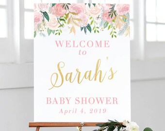 May include: A white welcome sign with pink and gold floral accents. The sign reads "Welcome to Sarah's Baby Shower April 4, 2019".