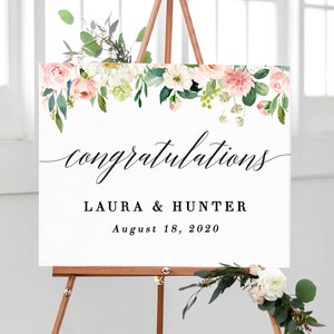 Puede incluir: Un cartel de bienvenida de boda blanco con un borde floral en tonos rosa y verde. El cartel dice "felicidades Laura & Hunter 18 de agosto de 2020".