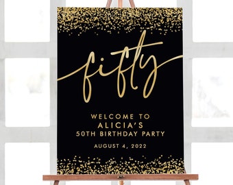 May include: A black and gold birthday party sign on a wooden easel. The sign features the word "fifty" in elegant gold script, with gold glitter accents at the top and bottom. Below, it reads "Welcome to Alicia's 50th Birthday Party August 4, 2022."
