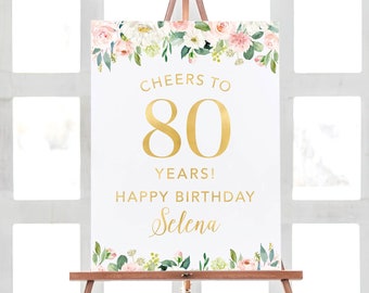 May include: White sign with gold floral border and text. The sign says "Cheers to 80 Years! Happy Birthday Selena".