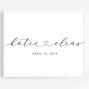 May include: A white framed print with the text "katie &hearts; elias" in black cursive script and the date "APRIL 14, 2019" below.