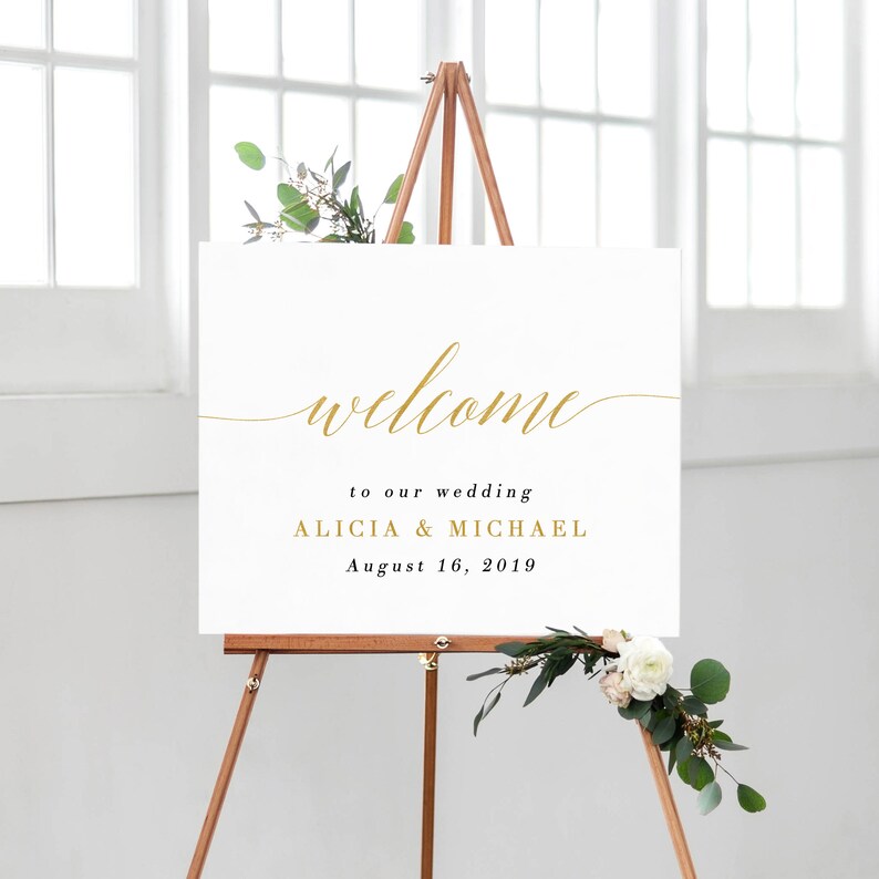May include: White wedding welcome sign with gold calligraphy lettering. The sign reads "welcome to our wedding Alicia & Michael August 16, 2019".