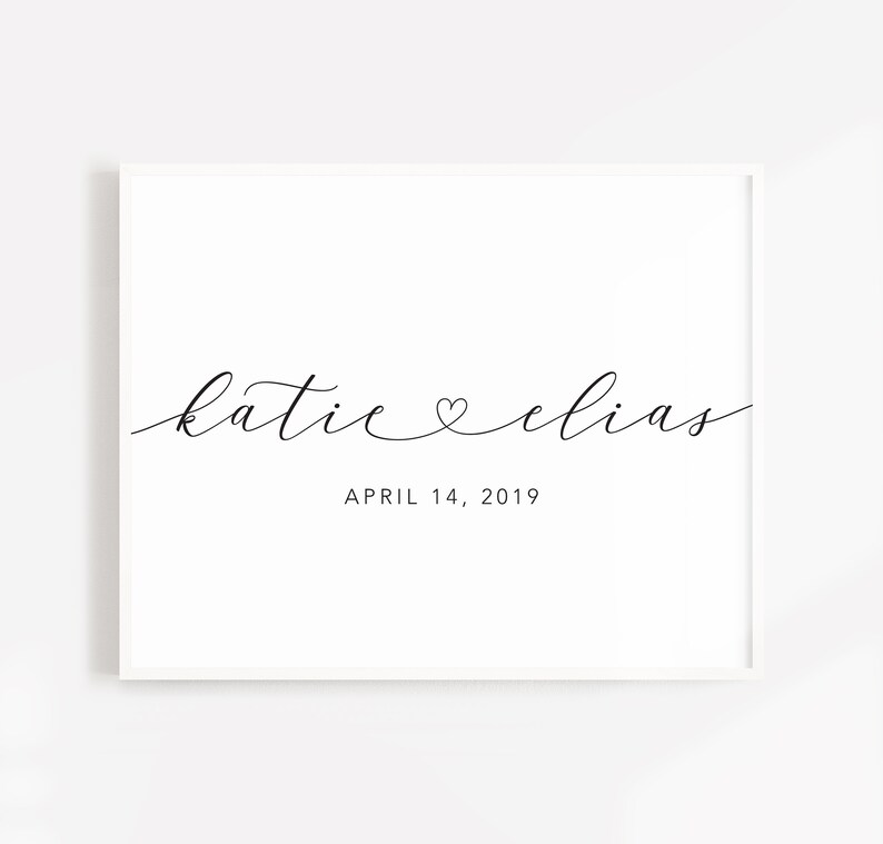 May include: A white framed print with the text "katie &hearts; elias" in black cursive script and the date "APRIL 14, 2019" below.